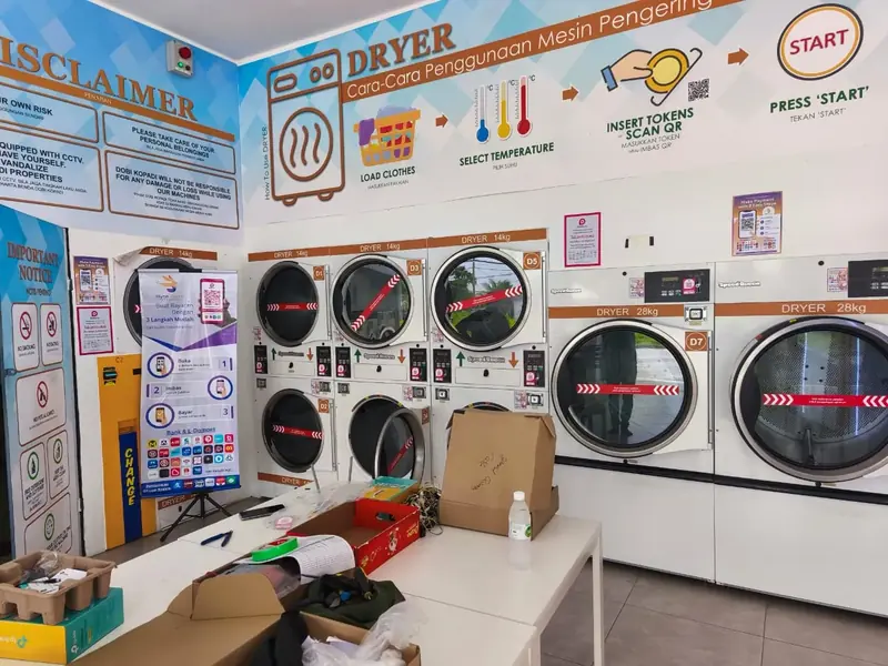 Laundromat dryers with QR stickers under the shop's wall sign: insert tokens or scan QR, then press start