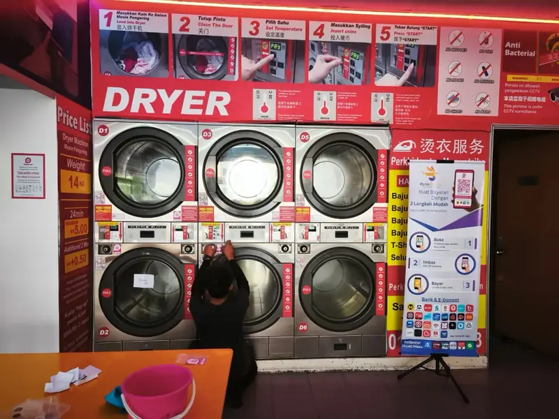A person fitting QR payment at a wall of stacked laundromat dryers, a Byte Bunny standee beside them