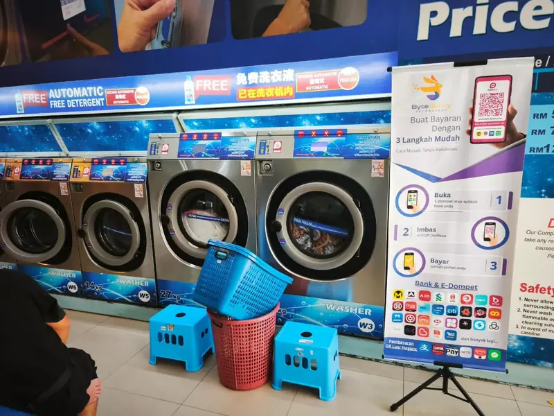 A row of self-service washers with QR stickers, a Byte Bunny standee showing the three payment steps and the banks and e-wallets
