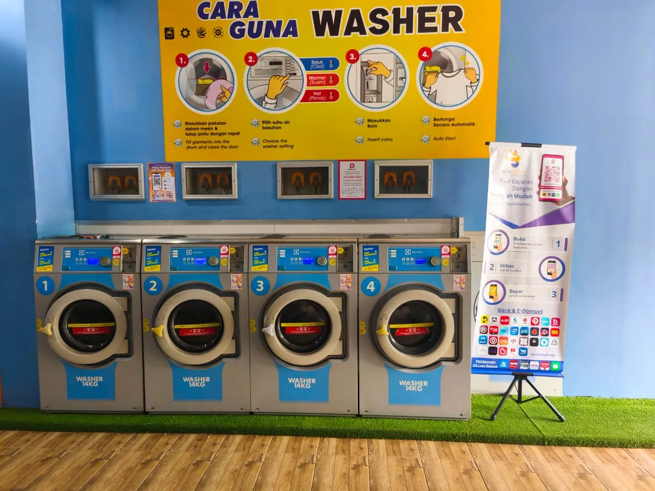 Four self-service washers with a DuitNow QR sticker on each, beside a Byte Bunny standee showing how to pay in three easy steps