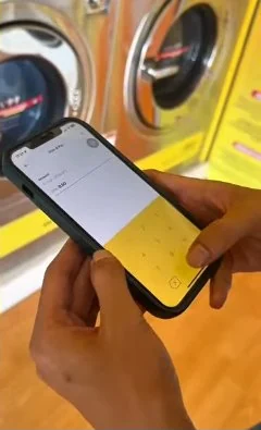 Frame from Byte Bunny's own washer film: thumbs entering the amount to pay in a phone app in front of the washers